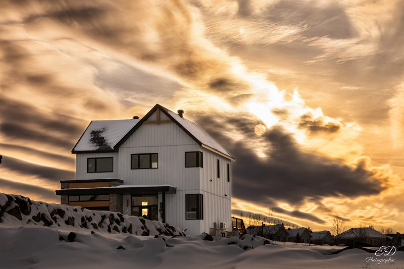 Vue d'une maison en hiver avec un soleil dans les nuages
